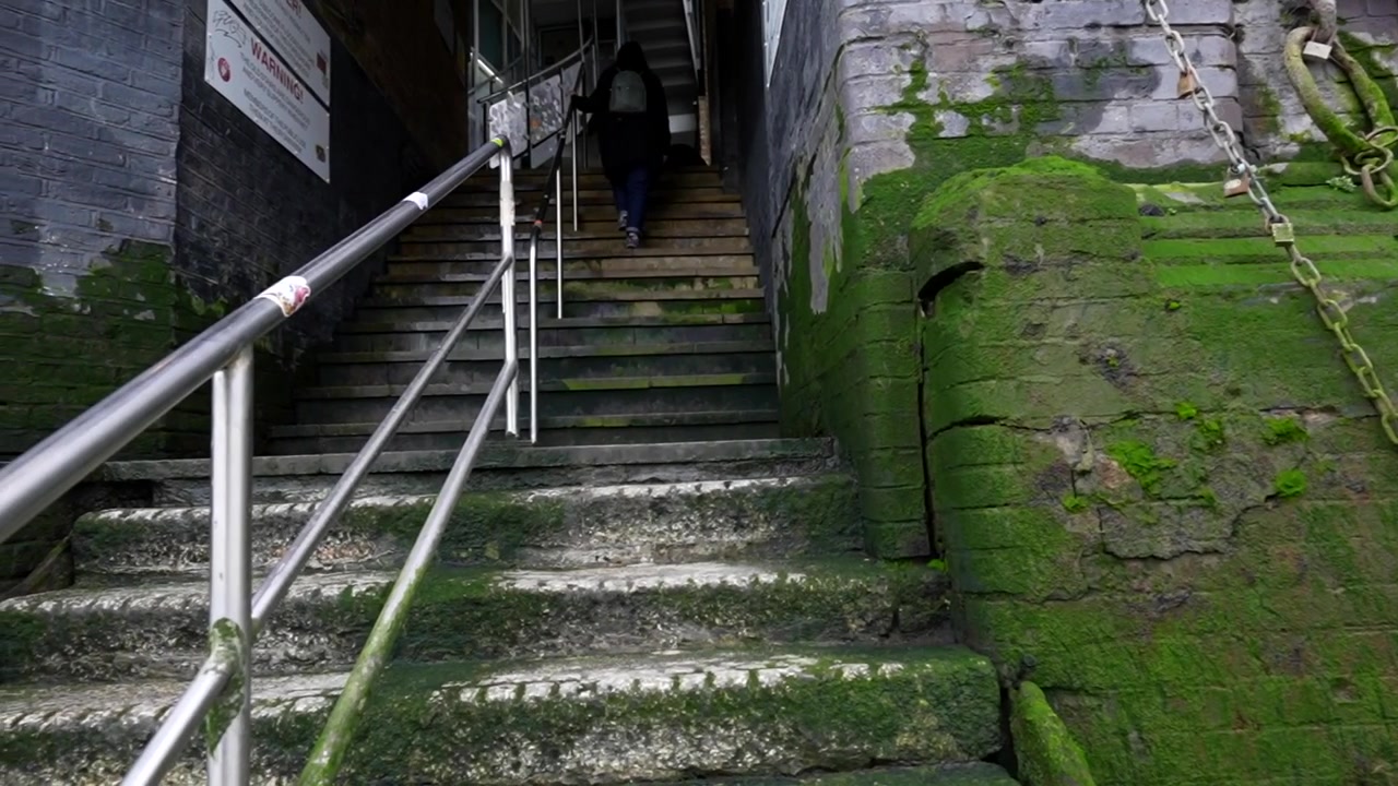 Woman climbing moss-covered stone steps affected by high tides along the Thames in London