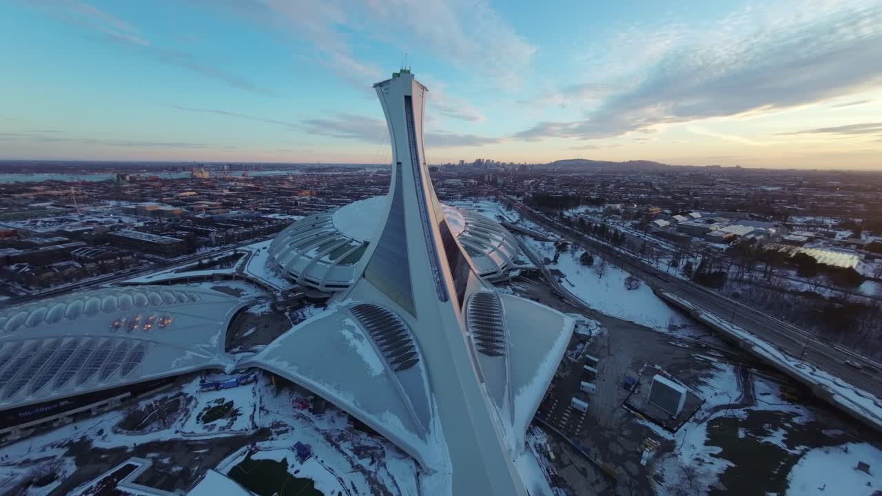 FPV drone’s wide sweep over Montreal Olympic Stadium at sunset, capturing snow-covered winter architecture