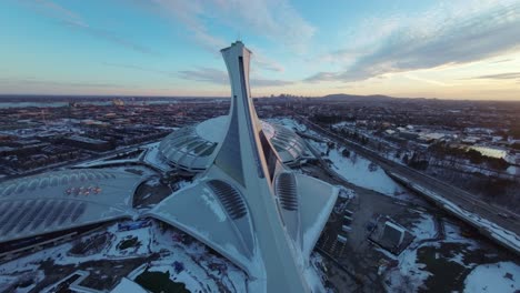 fpv drone’s wide sweep over montreal olympic stadium at sunset, capturing snow-covered winter architecture