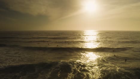 pacífico amanecer naranja aérea viendo las olas del océano rodar en la playa con surfistas siluetas en el océano pacífico