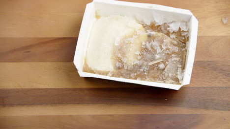 deep ice frozen packed retail food in a meal box container being thrown on a wooden table