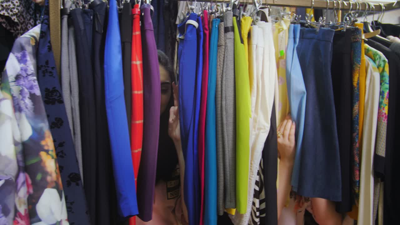 Two Friends Hiding Behind Clothes in a Clothing Store