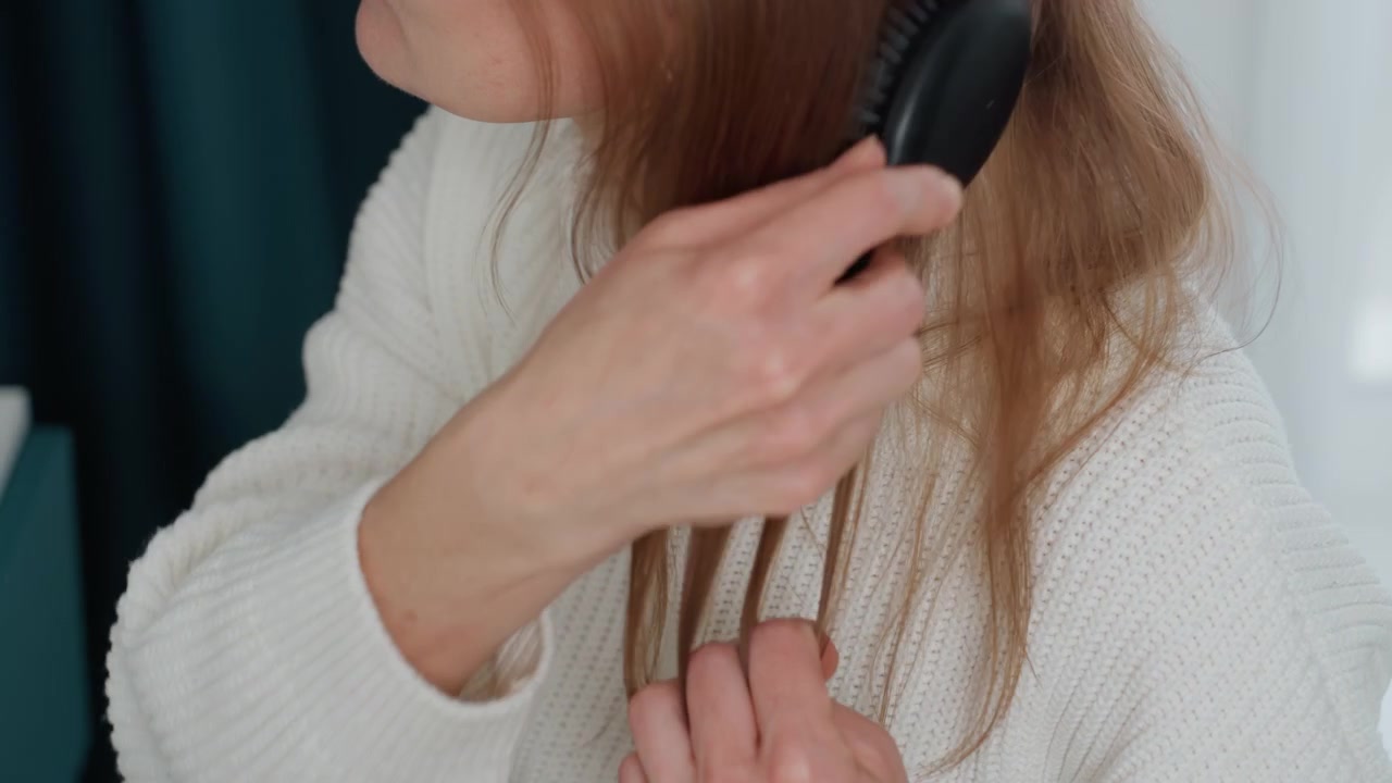 Caucasian woman coach detangling hair before virtual coaching session, closeup on hands and profile, checking split ends and frizz, anxious glance toward mirror, candid home routine preparing