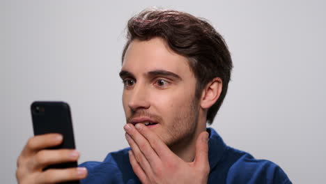 Shocked-man-reading-news-on-smartphone-in-studio.-Guy-using-mobile-phone