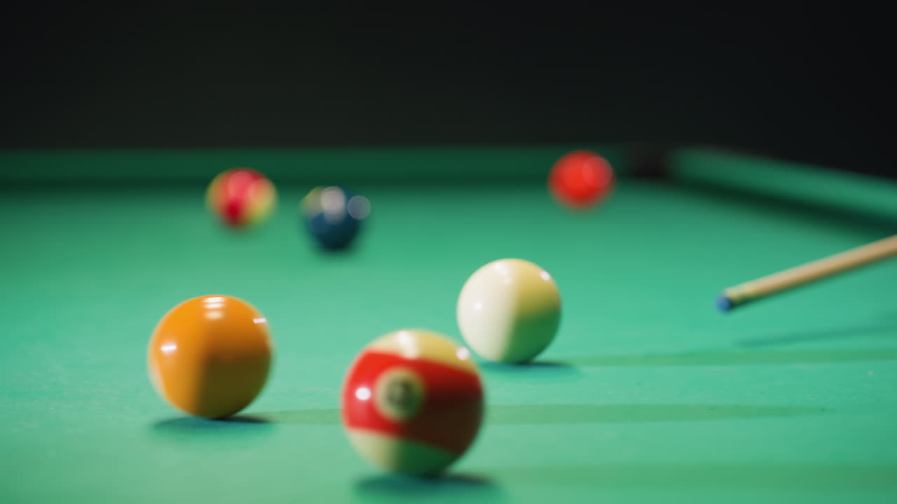 Close-up view of colorful billiard balls scattered on green pool table as white ball strikes orange ball. Vibrant scene captures movement, precision, and dynamic energy of strategic gameplay