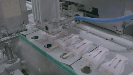 ice cream lollies on sticks moving along food production assembly line with surrounding machinery