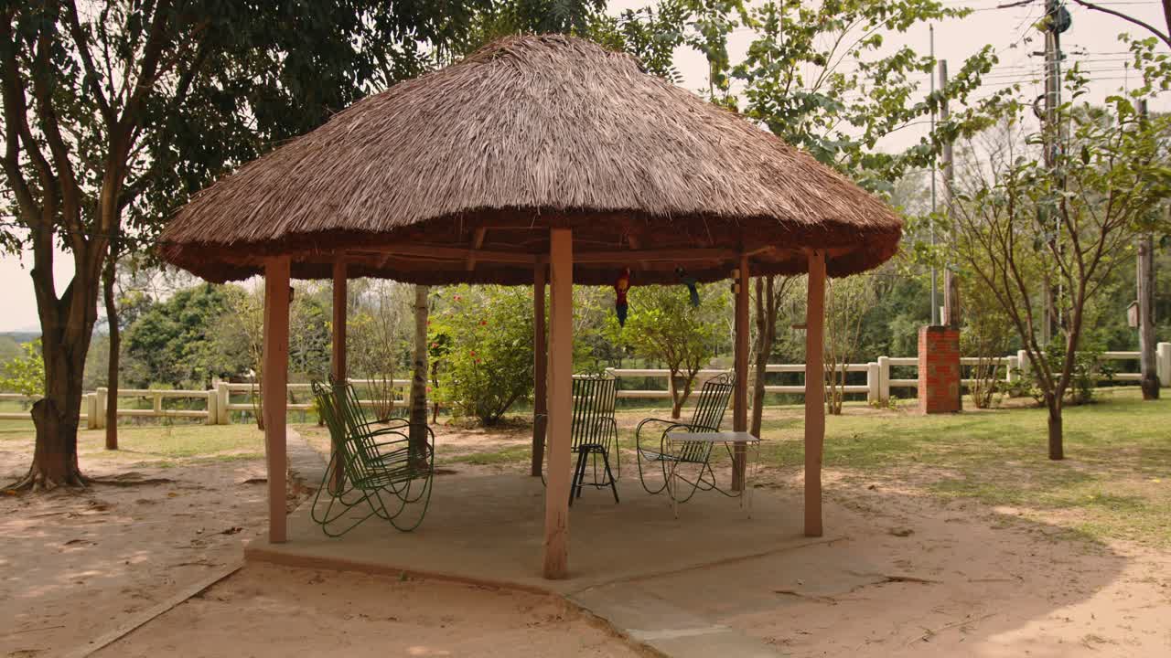 Stråtækt lysthus ved et landsted i Paraguay, med grønne jernstole under, på en smuk, rolig og afslappende morgen, ferie.