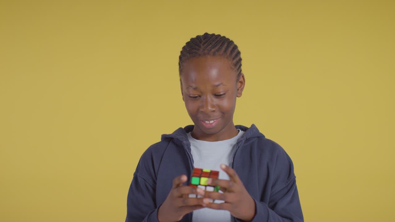 Studio Portrait Of Young Boy On ASD Spectrum Solving Puzzle Cube On Yellow Background 1