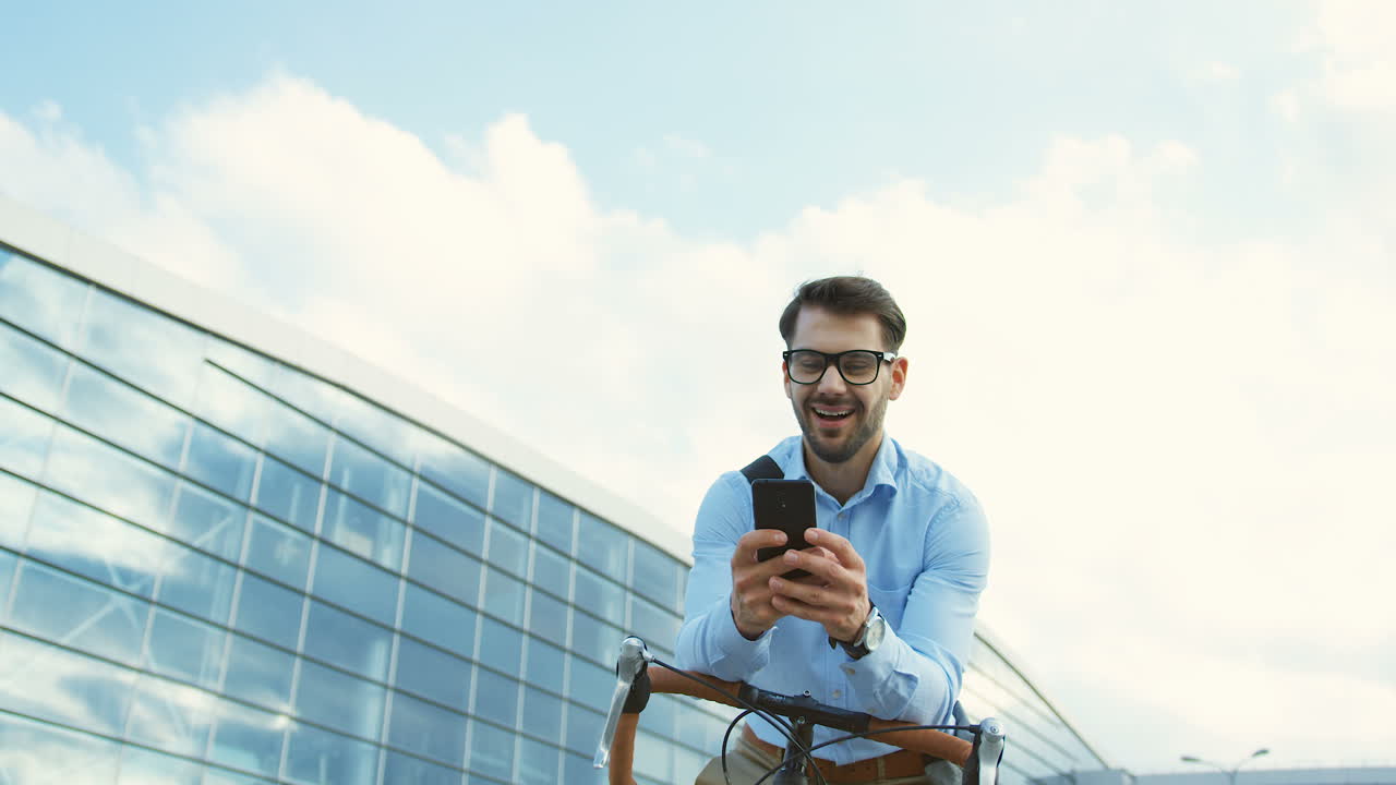 Handsome man wearing glasses, laughing while having a chat and typing a message on smartphone