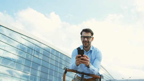 Hombre-Guapo-Con-Gafas,-Riendo-Mientras-Conversa-Y-Escribe-Un-Mensaje-En-El-Teléfono-Inteligente