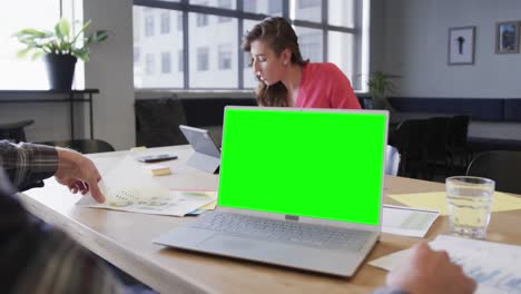 Opened-laptop-with-green-screen-on-desk-in-office