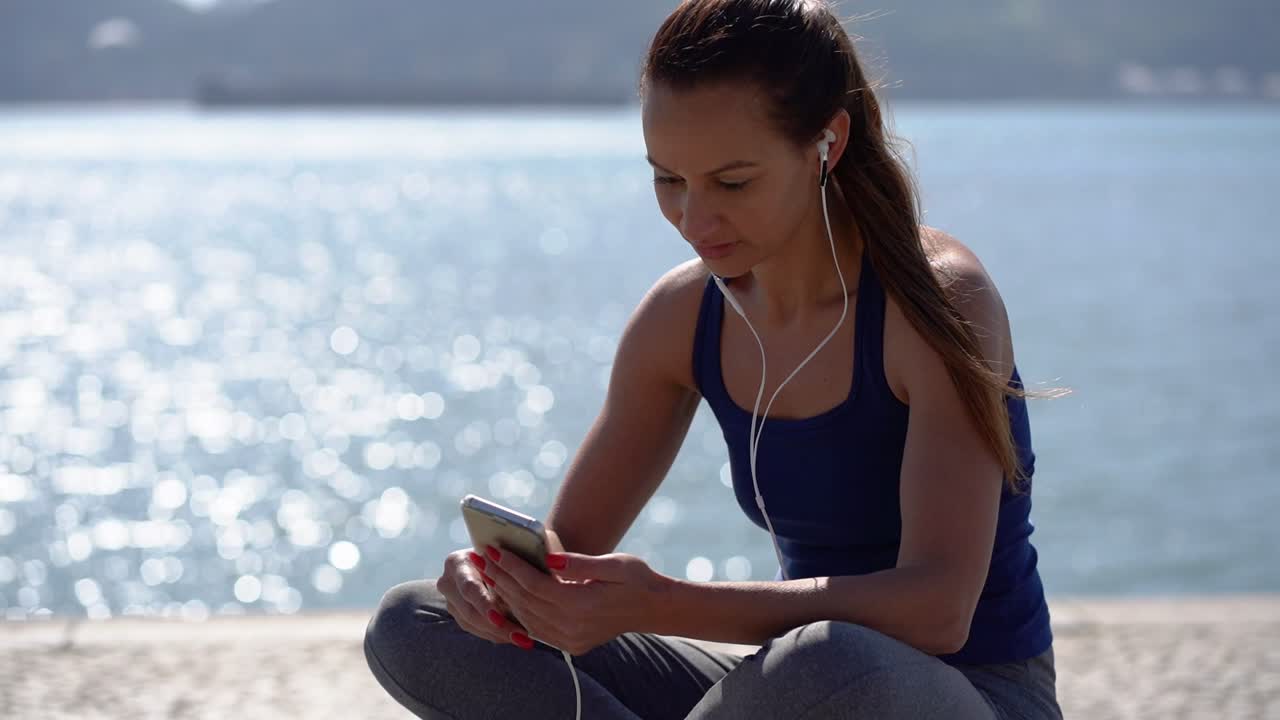 chica deportiva sentada y escuchando música con un teléfono inteligente al aire libre