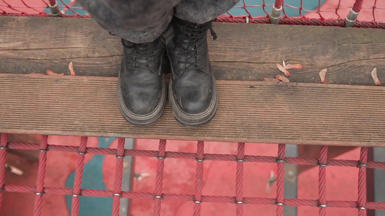 Muddy boots on weathered plank above red metal grating, deckhand pausing on pier, salt spray on leather, overcast reflection in water below, steady stance and rugged texture, nautical solitude