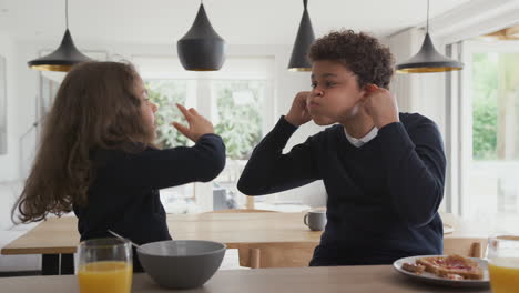 niños en el mostrador de la cocina comiendo el desayuno y haciendo caras antes de ir a la escuela