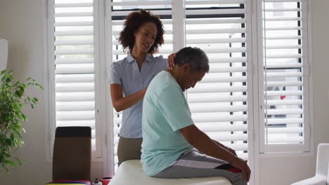 Physiotherapeutin-Gemischter-Abstammung-Hilft-Einem-älteren-Mann,-Seinen-Rücken-Zu-Massieren