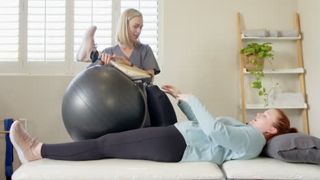 physical therapist assisting woman with prosthetic leg using exercise ball in clinic