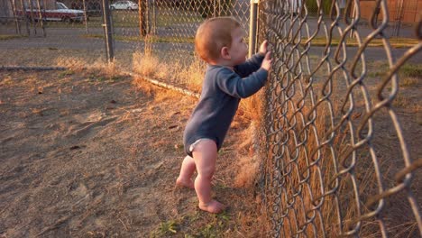 happy toddler boy stands against fence near home plate and shakes fence