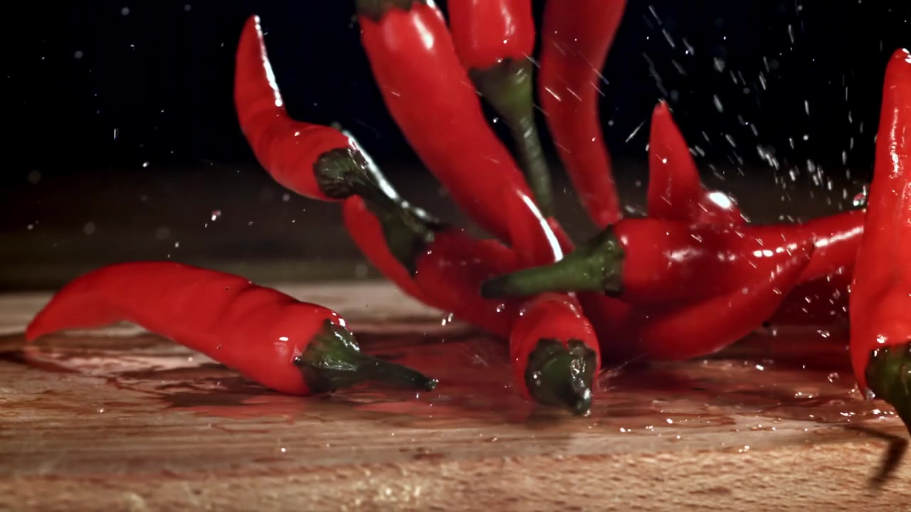 Slow Motion Red Chili Peppers Falling onto Wet Wooden Surface
