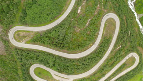 top down view of winding forest road in green mountain woods in stryn, norway - aerial drone shot