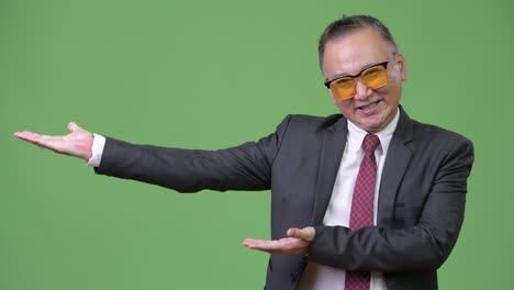 un hombre de negocios japonés maduro con gafas de sol contra un fondo verde.