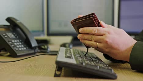 a businessman man with an empty wallet without money in his hands is working on a computer keyboard at an office desk, close-up