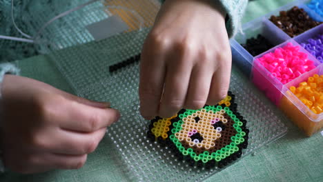 closeup of a female making a colourful babushka design from ironing beads