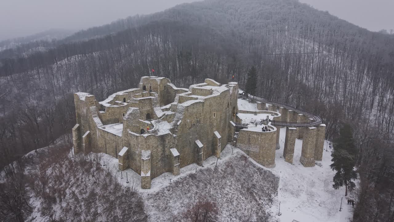 Drone footage of Neamt Fortress covered in snow, surrounded by forested hills in winter