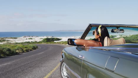 mujer afroamericana con gafas de sol sentada en el coche descapotable en la carretera