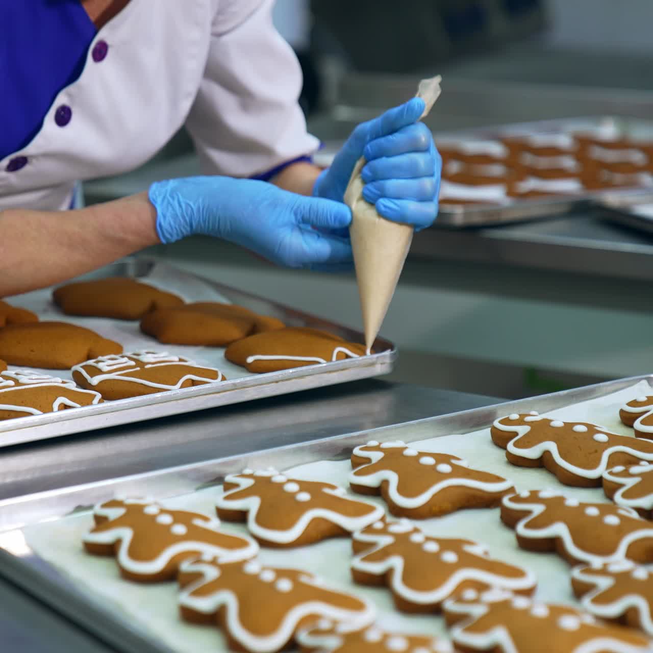 Worker squeezing icing cover on cookies from a pastry bag. Decorating gingerbread sweets on a confectionery factory. Trays with cookies in blur at background