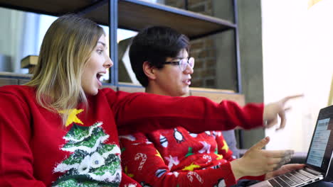 una pareja con suéteres de navidad trabajando juntos en una computadora portátil