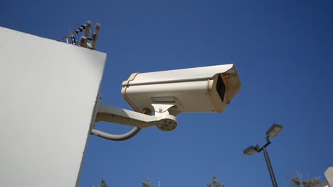 Close-Up-White-Surveillance-Camera-With-Blue-Sky-in-Background