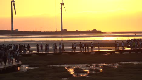 Beautiful-orange-sunset-landscape-shot-overlooking-at-tourist-crowds-movement-on-the-platform-at-pristine-attraction-Gaomei-wetland-preservation-area,-Taichung-city,-Taiwan