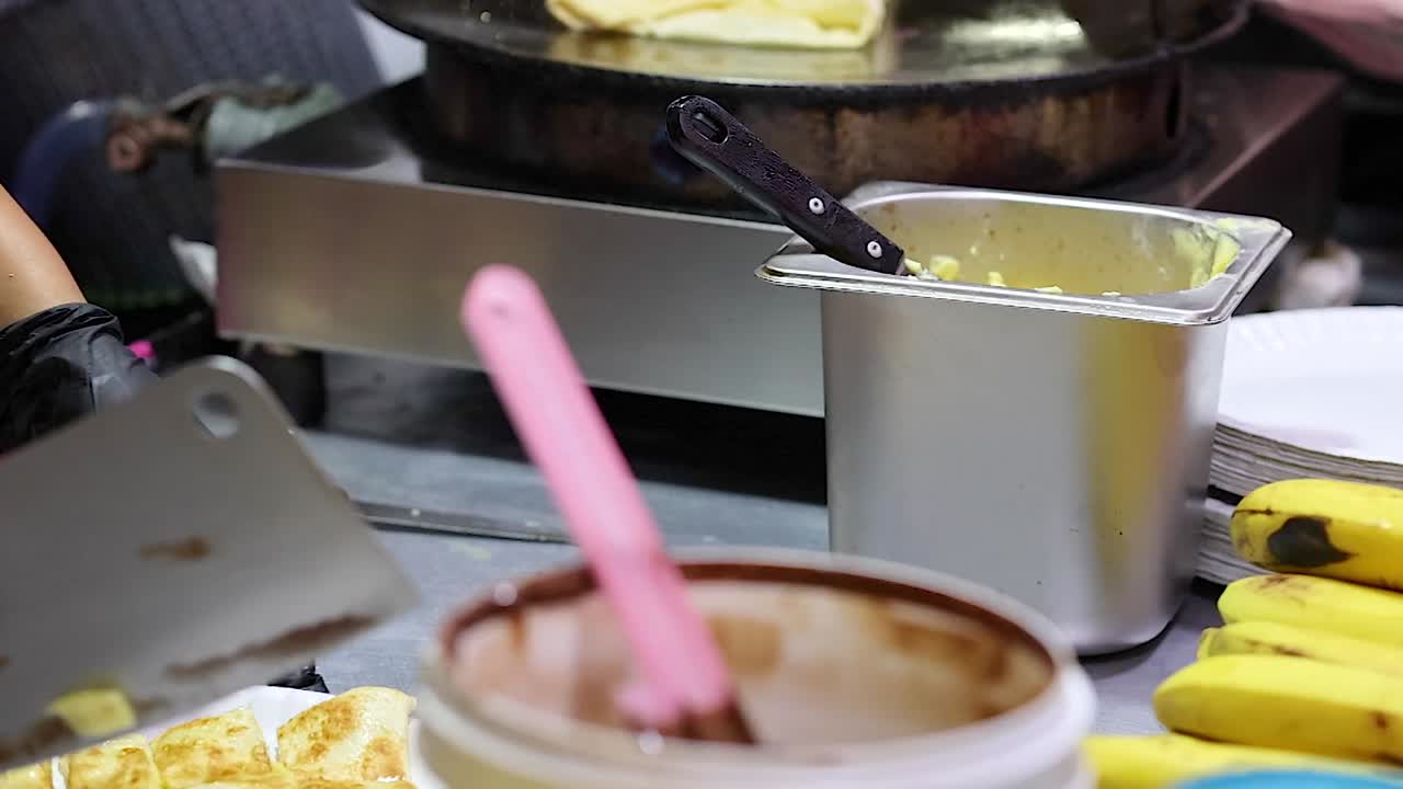 Un venditore ambulante di street food con guanti neri serve roti di banana a fette su un piatto
