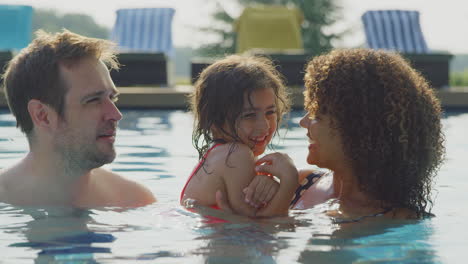 mother and father having fun in swimming pool on summer vacation with daughter