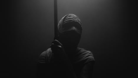 a mummified woman against the dark background pose with the walking staff