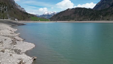 Aerial-forward-view-of-shoreline-of-an-alpine-lake-in-a-fantastic-mountain-landscape