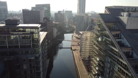 aerial drone flight above the rooftops along the river irwell in manchester city centre shoing a sunny and hazy view of the skyline