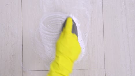 the human hand in yellow protective glove cleans the ceramic wall or floor, making circular motions with brush and soap cleanser or detergent and trying to wipe out the dirty. housekeeping concept.