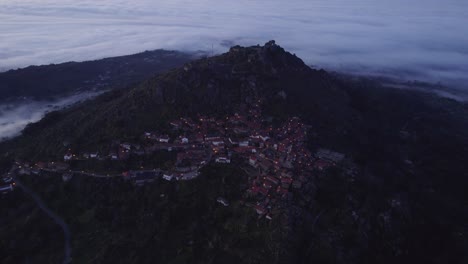 Toma-Panorámica-Lateral-Del-Pueblo-De-La-Cima-De-La-Colina-Monsanto-Portugal-Con-Nubes-Bajas-Durante-El-Amanecer,-Antena