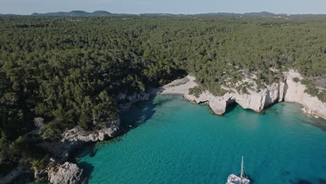 Sailing-yacht-floating-off-the-coast-around-Cala-Mitjana-beach-in-Menorca-displaying-a-European-summer-day
