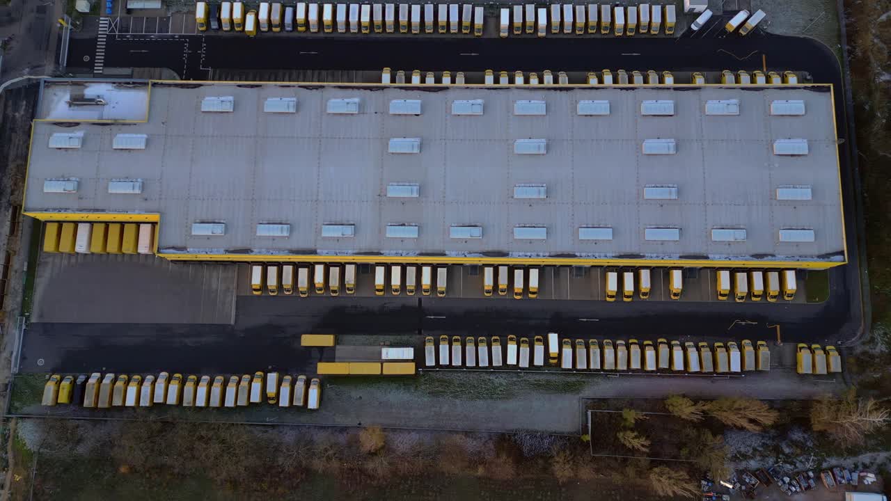 Large warehouse facility with numerous trucks parked at loading docks, representing global distribution. Breathtaking aerial view drone camera pointing down