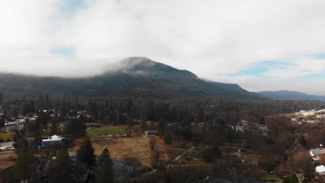 Luftabstieg-über-Kleine-Bergstadt,-Wolkenbedeckter-Berg-Im-Hintergrund