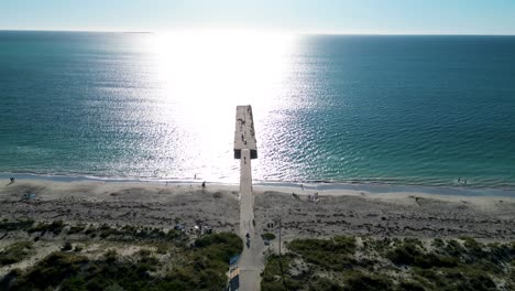 Aerial-drone-backward-moving-shot-over-tourists-walking-towards-Coogee-Beach-Jetty-in-Perth,-Western-Australia-during-evening-time