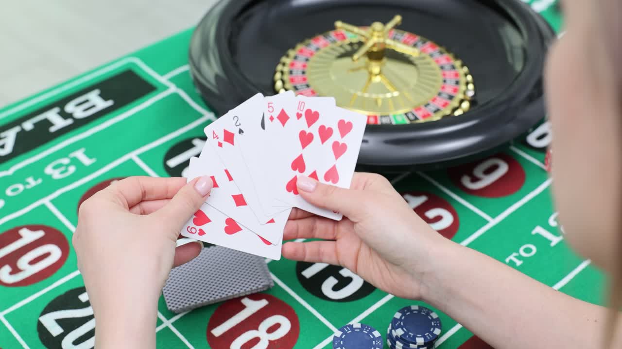 Close-up of hands holding playing cards at a casino table with a roulette wheel and chips