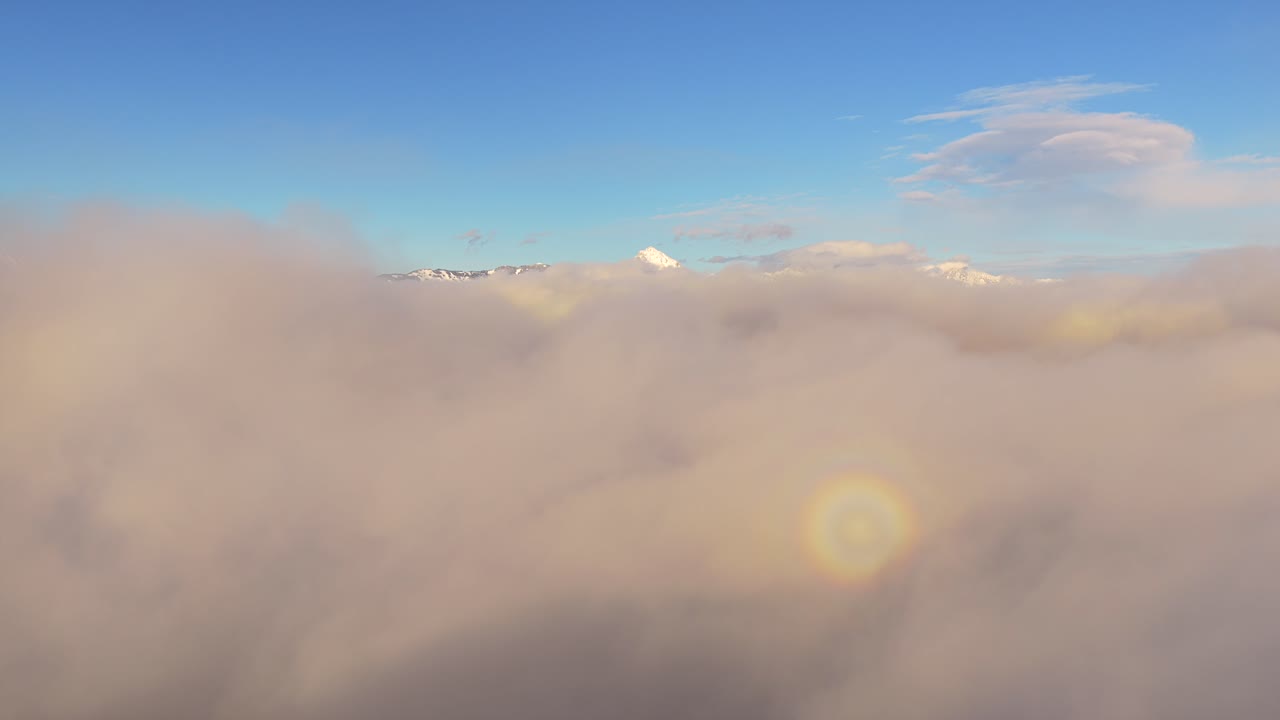 Aerial view above clouds, distant snow-capped Julian Alps peaks visible