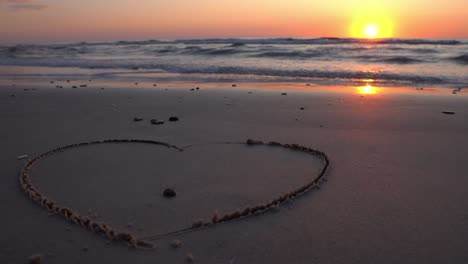 símbolo de corazón dibujado en la arena contra un telón de fondo de puesta de sol sobre el mar