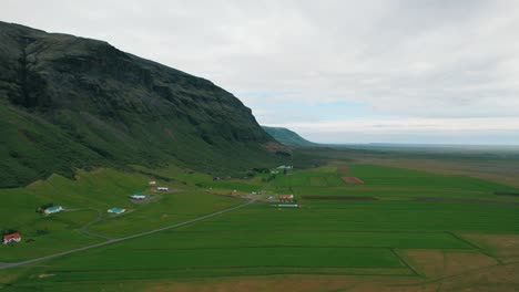 the slope of a huge green rock with a few houses next to it