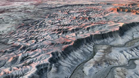 Sun-capped-mountain-peaks,-aerial-over-big-grey-desert-panorama-in-sunset-light