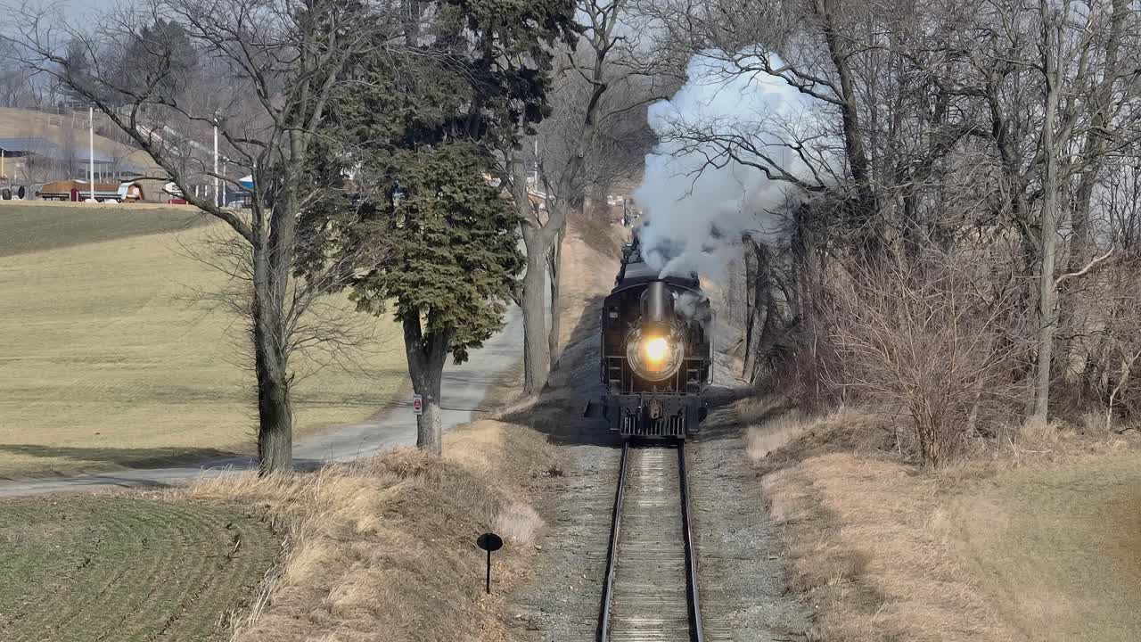 A historic steam train travels through a rural winter landscape surrounded by leafless trees and open fields vibrant colors stunning visuals atmospheric lighting