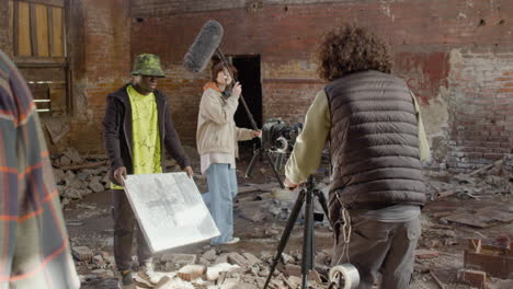 cameraman setting up a camera in a ruined building while another coworker showing a gleaming banner in front of the camera 1